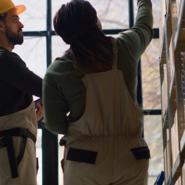 Hip level shot of warehouse manager and trainee performing inventory check, keeping quality standards high. Proactive experts in depot prepare to ship parcels, crosschecking delivery info
